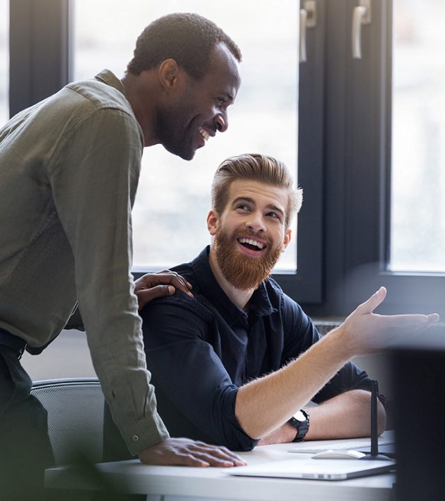 Two happy smiling men working together on a new business project at a workplace